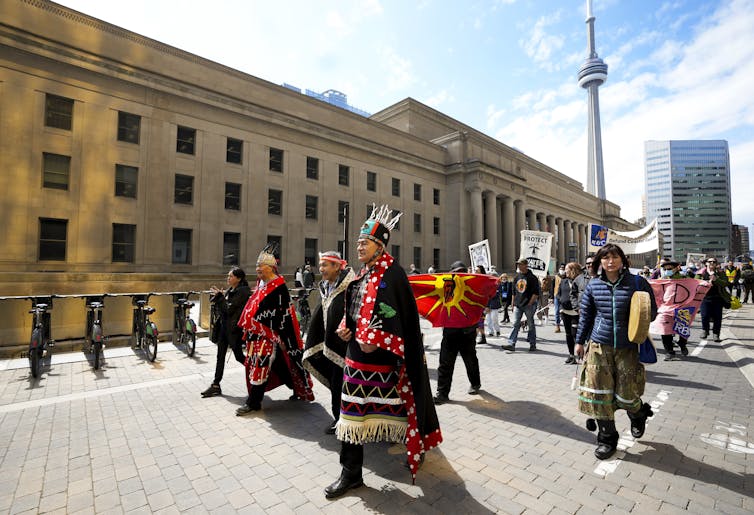 Wet'suwet'en chiefs march along a city street with the CN Tower in the background.