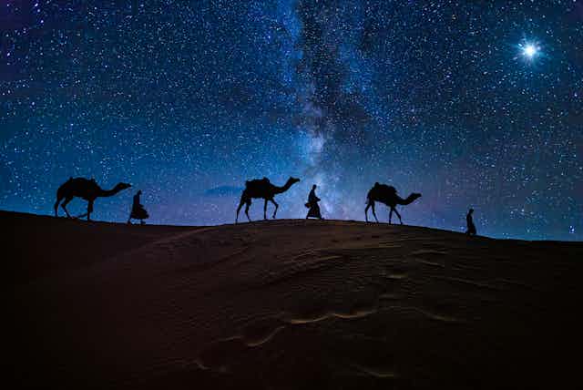 Ilustração mostra três homens e seus camelos atravessando deserto à noite seguindo uma estrela brilhante