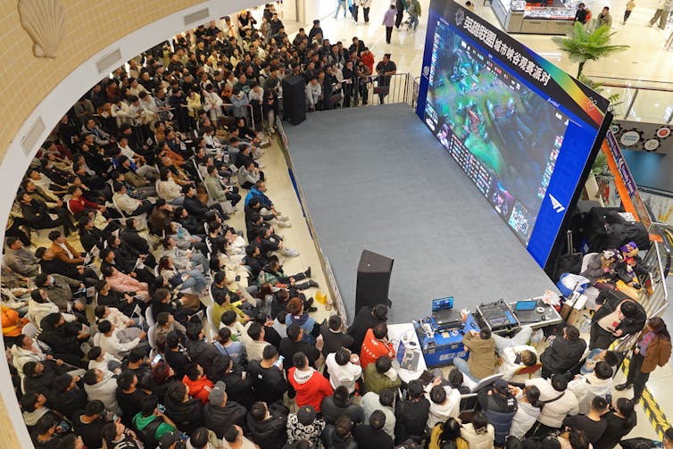 People crowd into a curved atrium around a giant screen.