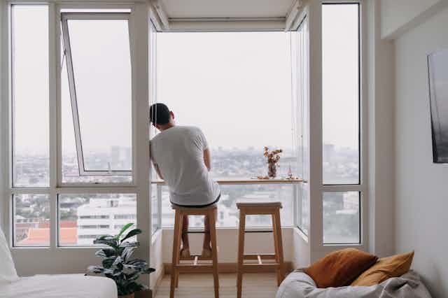 a man sits alone in an apartment looking out of the window.