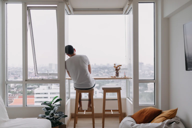 a man sits alone in an apartment looking out of the window.