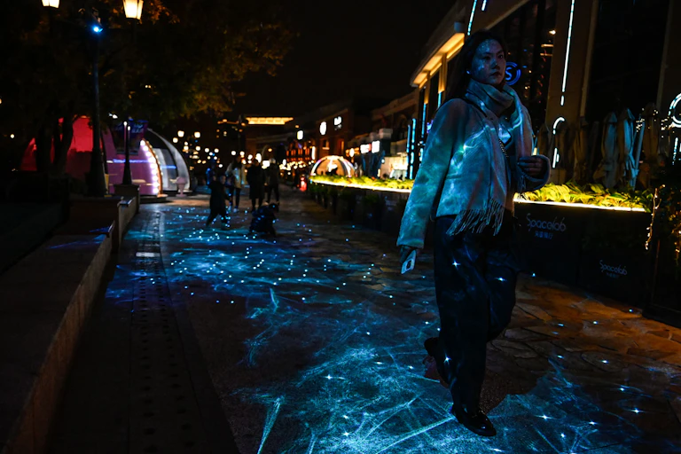 A woman strides along a passage bathed in colored lights