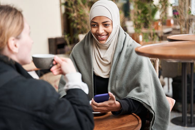 Two women are chatting over coffee.  One wears a hijab.
