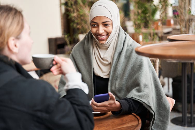 Two women chatting over coffee. One wears a hijab.