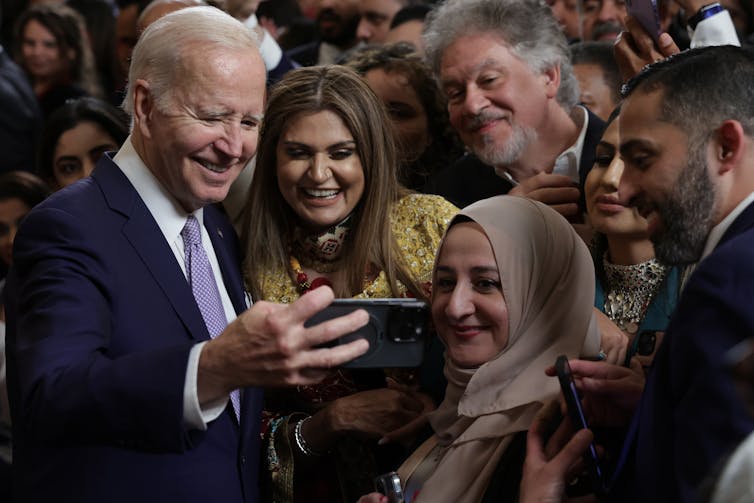 A middle aged white man wearing a business suit is taking a picture of people celebrating a holiday.