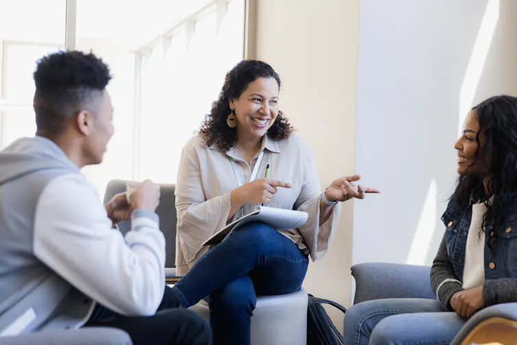 Two teens -- one male and one female -- speak with a counselor. They're all smiling.