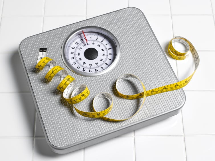 Tape measure lying on top of a scale on a white tile background.