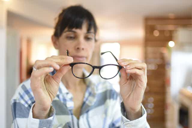 A woman holds a pair of black-framed glasses.