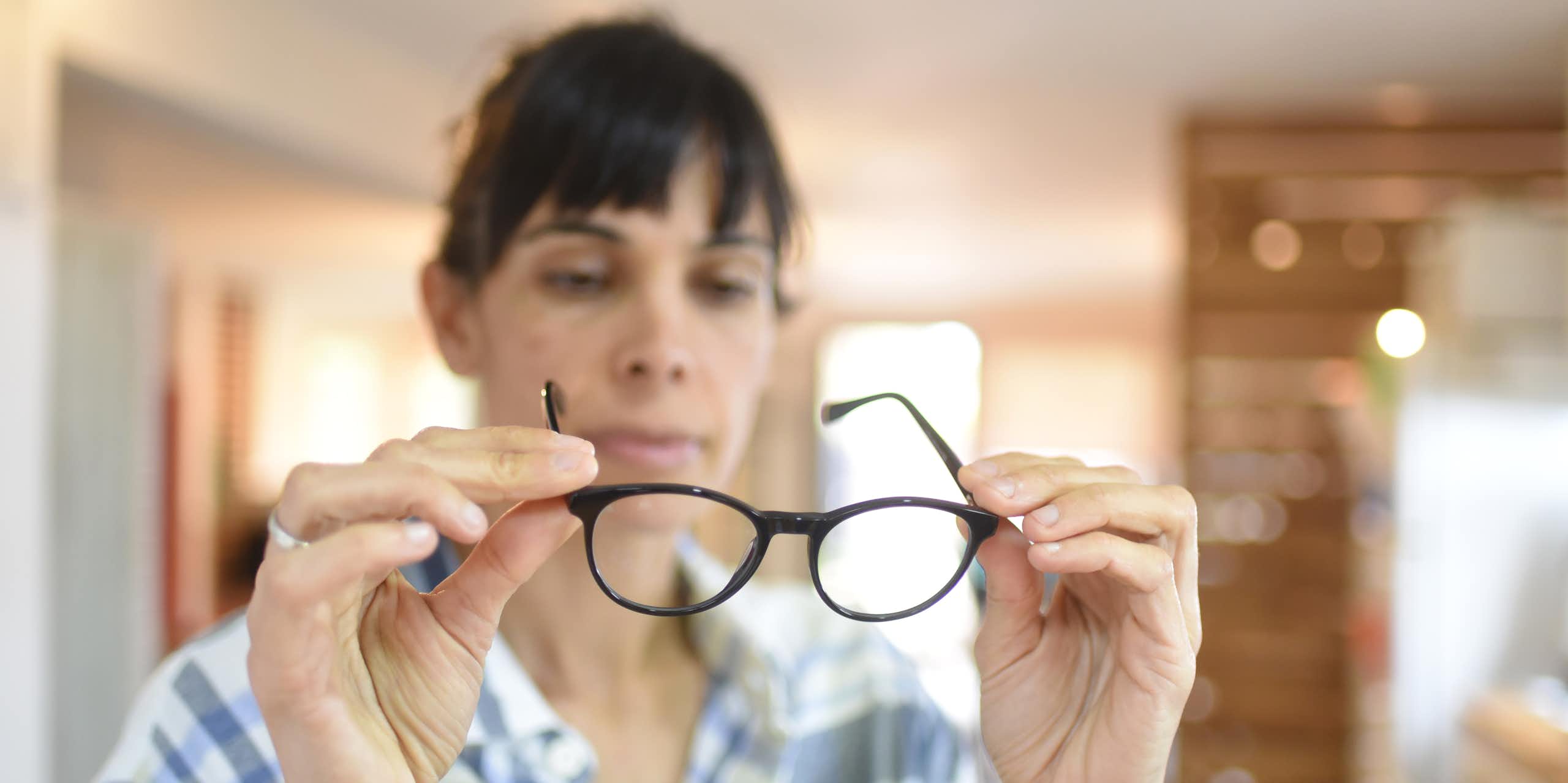 A woman holds a pair of black-framed glasses.