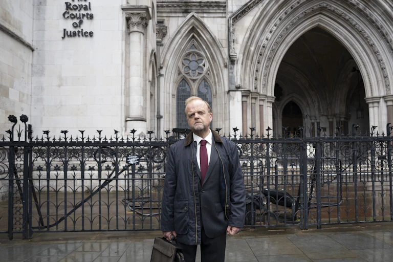 Man stands outside a court holding a suit case.
