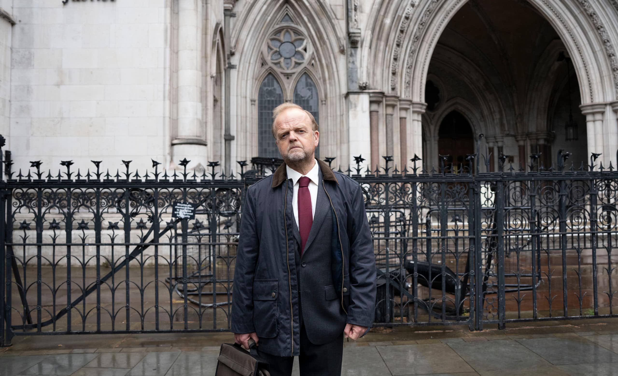 Man stands outside a court holding a suit case.