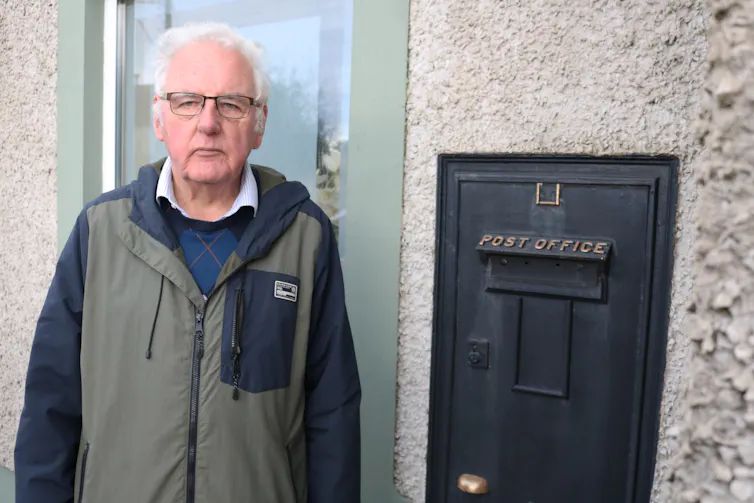 Grey-haired man next to a letter box.