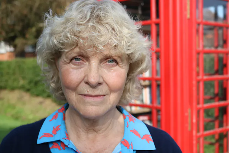 Woman stands in front of a red telephone box.