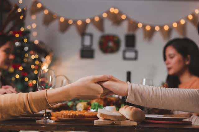 Women eat together and hold hands, Christmas decorations in the background.