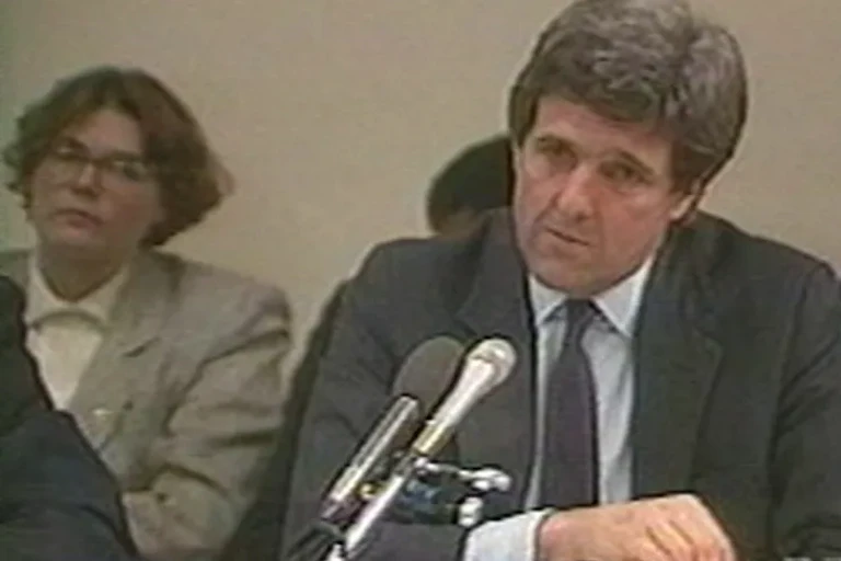 Screen grab from grainy video of man in suit seated before a microphone flanked by a young woman and a young man.