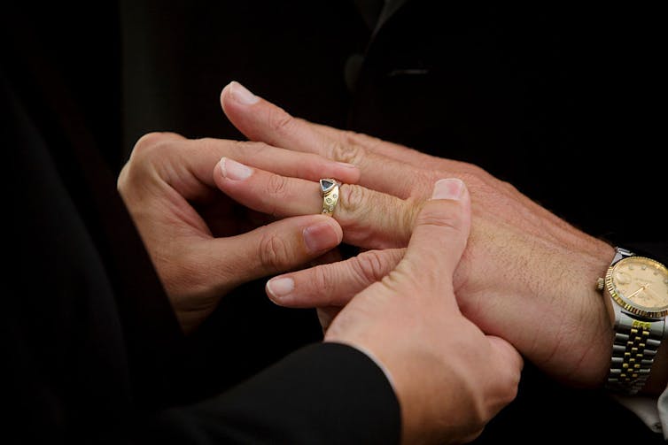 A close-up shot of one person's hands slipping a gold and blue ring onto another person's finger.