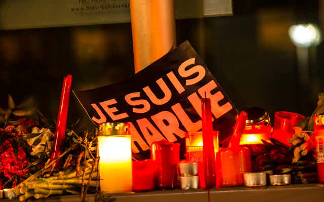A sign reading Je Suis Charlie as part of a memorial on the ground, surrounded by flowers and lit candles