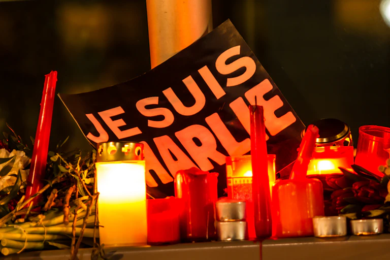 A sign reading Je Suis Charlie as part of a memorial on the ground, surrounded by flowers and lit candles