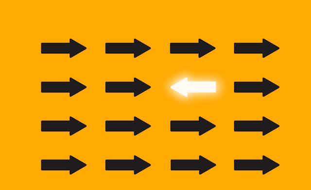 One illuminated arrow points to the left in a sea of black arrows pointing to the right.