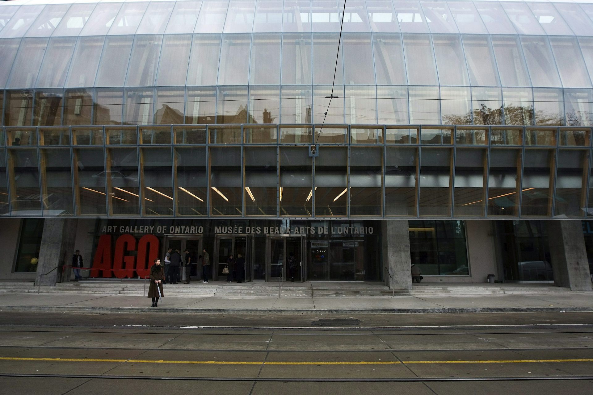 A person with umbrella seen in front of a building with wide steps and many glass panes that says Art Gallery of Ontario.
