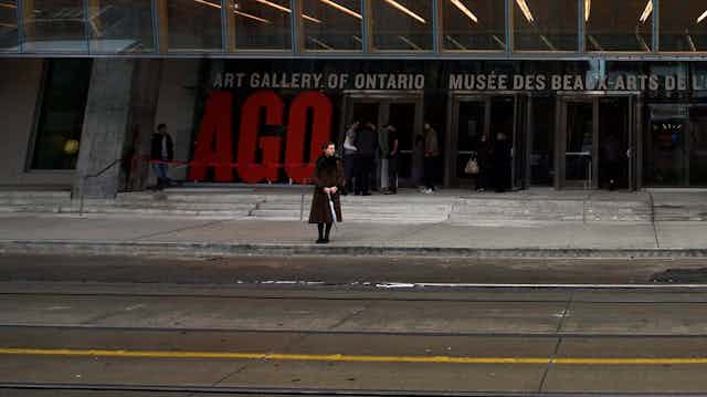 A person with umbrella seen in front of a building with wide steps and many glass panes that says Art Gallery of Ontario.