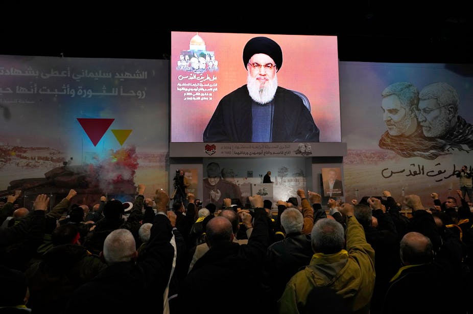 Hezbollah supporters cheer leader Hassan Nasralleh as he delivers a speech on a video screen.