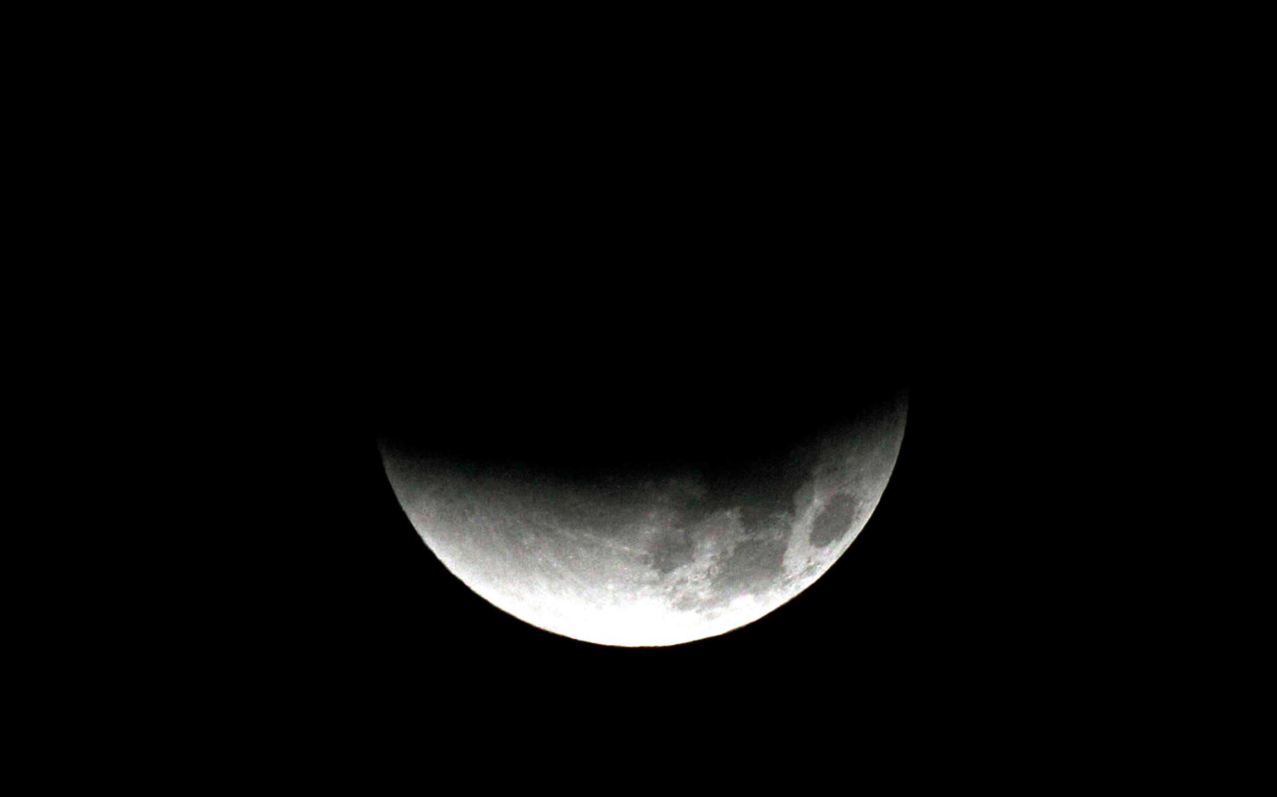 The moon, partially shadowed on the top side, against a dark background.