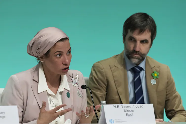 Two people sit next to each other in front of a green screen