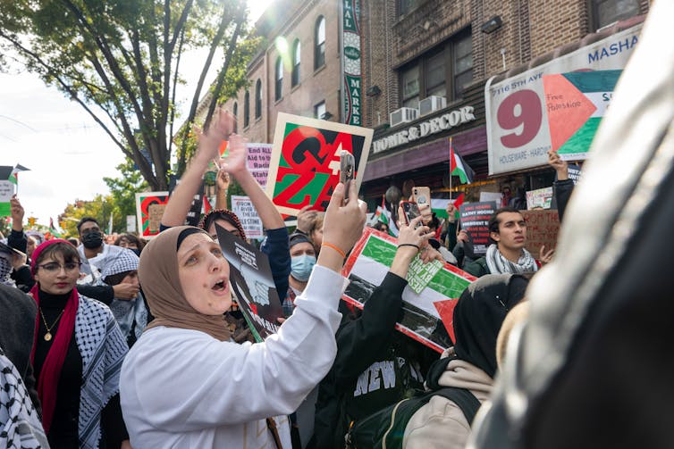 Una mujer que lleva un paño religioso sobre su cabeza se encuentra en medio de una multitud de personas que sostienen un cartel que dice Gaza.