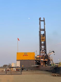 A tall steel drilling rig and a large yellow container, with a red flag on top of the container.
