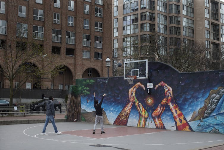 Two young people playing basketball on an urban court with a mural