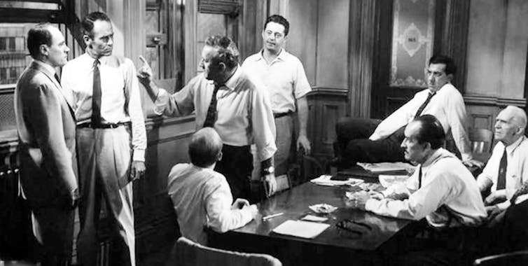 Black and white photo of men standing up or sitting around a table