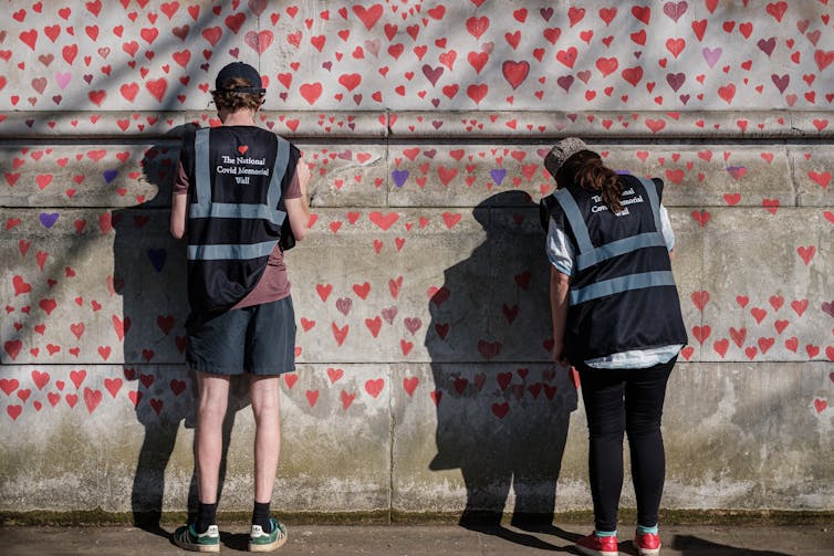 Workers add red hearts on the Covid memorial wall in London.