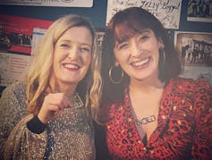 Two smiling women, one holding out her necklace to the camera.