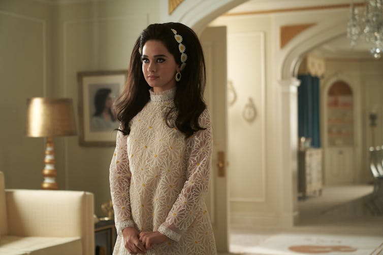 Priscilla stands in the house in a white dress and dyed black hair.