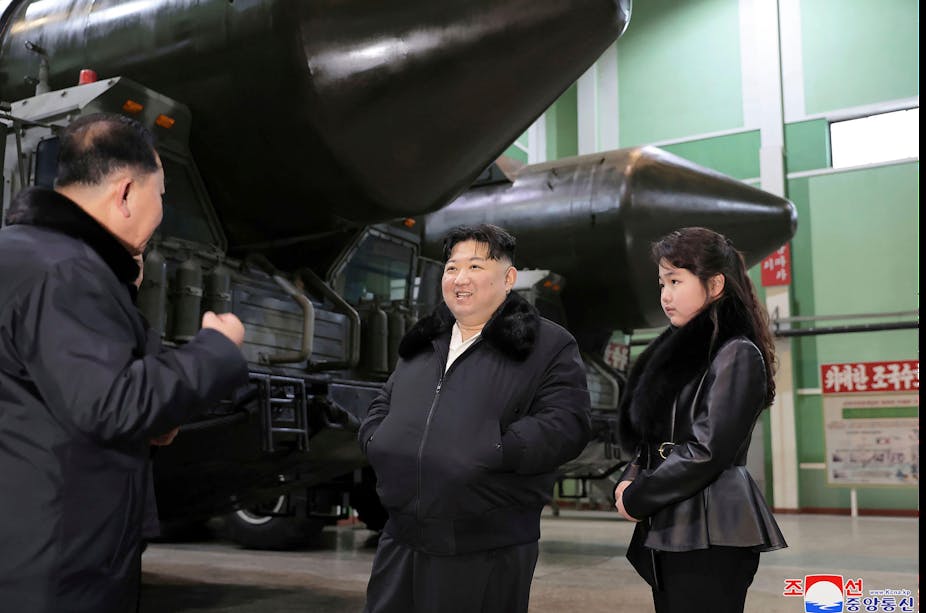 Kim Jong Un and his daughter stand next to large missiles.