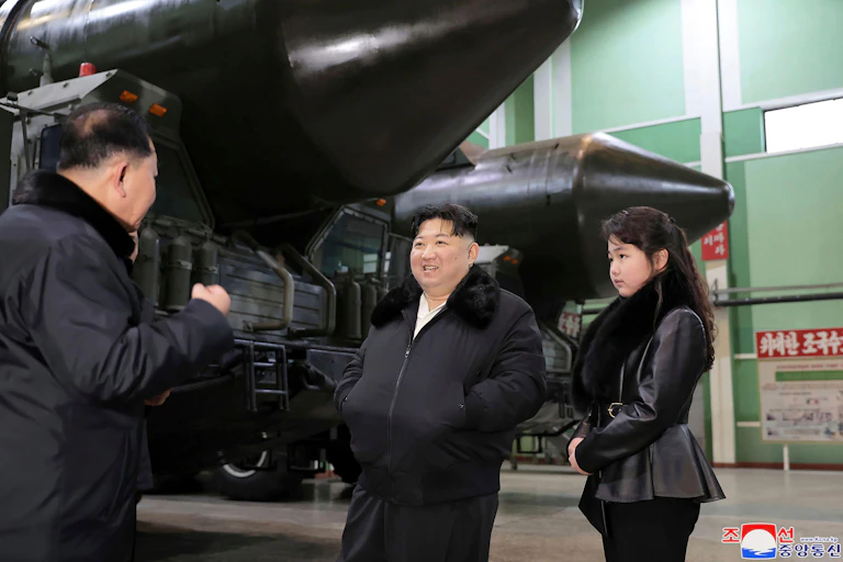 Kim Jong Un and his daughter stand next to large missiles.