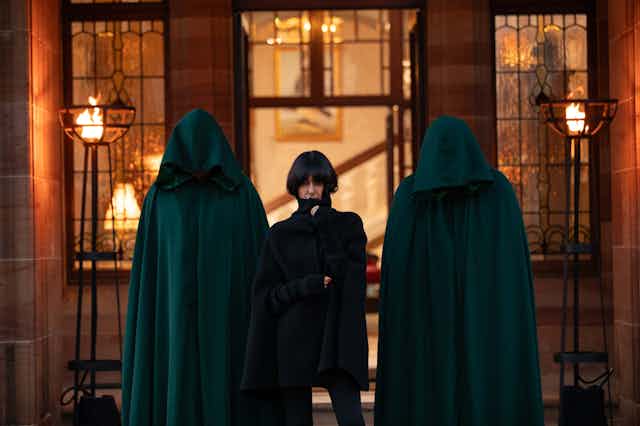 Two hooded figures and Claudia Winkleman