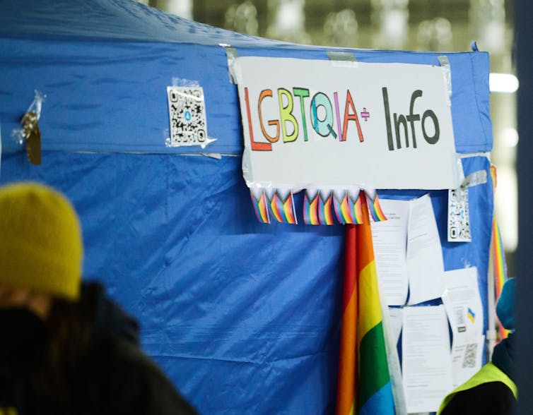 A sign reading 'LGBTQIA+ Info' is taped to a blue tarp.