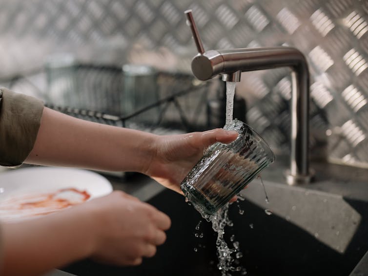 A person washes a glass in a sink, with dirty dishes on the side.