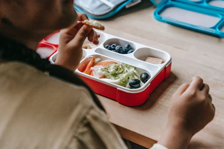 A student eats from a lunchbox containing green salad, crackers and blueberries.