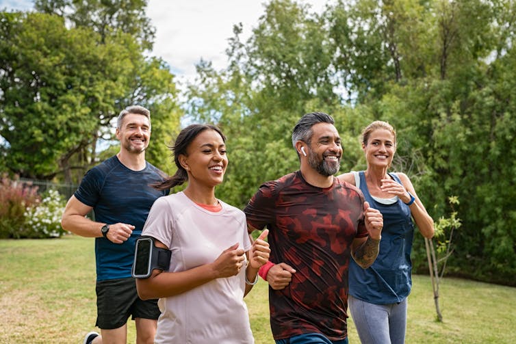 A group of two men and two women run together in a park.