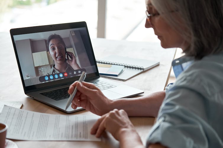 Woman speaks to female colleague (kitchen in the background) via zoom.