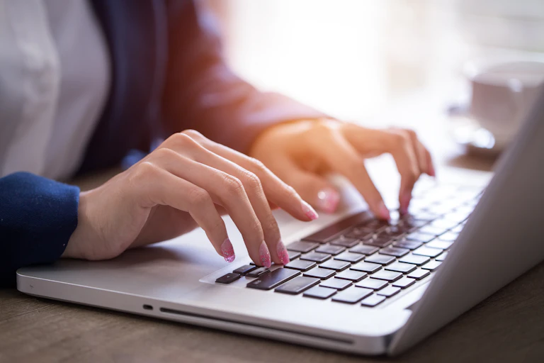 A woman's hands are seen typing on a laptop computer.