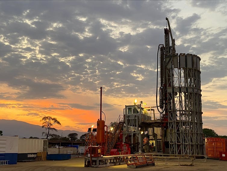 A large metal structure next to a truck and a cylindrical red tank, with the setting sun in the background.