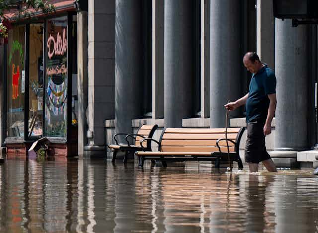 A man with his pants rolled up to his knees and a stick to check the water depth walks through shin-high water in downtown.