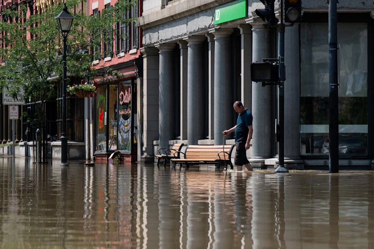 A man with his pants rolled up to his knees and a stick to check the water depth walks through shin-high water in downtown.