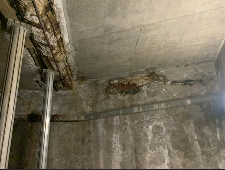 A basement with metal clearly showing through the cracked cement on the ceiling.