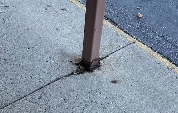 A rusted steel beam sticking up through a cracked sidewalk.