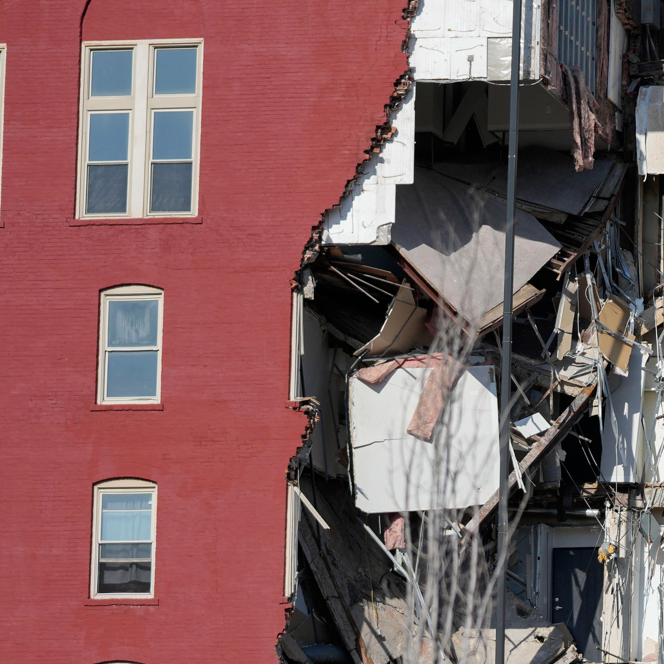 Several floors of a red brick six-story apartment building are gone. Clothing is still visible in closets.